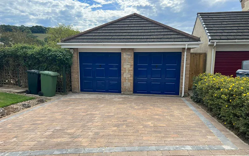 A brick driveway with two blue garage doors.
